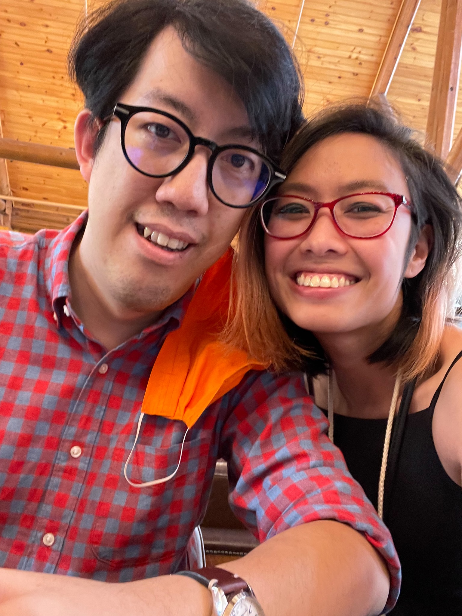 Selfie of Andy and Michelle in Gatlinburg, Tennessee. Andy is wearing a pink and blue checkered button-down shirt, with an orange face mask hanging from his ear. Michelle is wearing a black tank top with a navy face mask hanging from her neck.